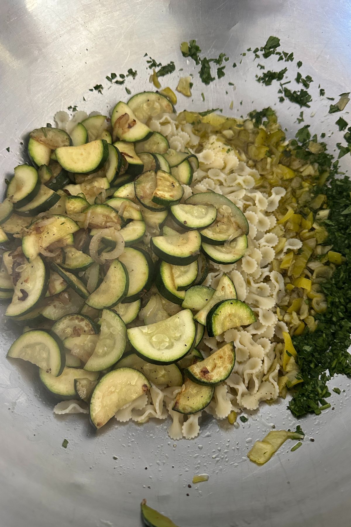 Combining pasta, zucchini, walnuts, and vinaigrette in a mixing bowl