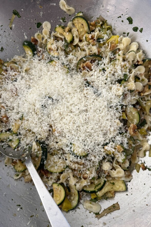 Tossed arugula pasta salad in large bowl with Parmesan cheese