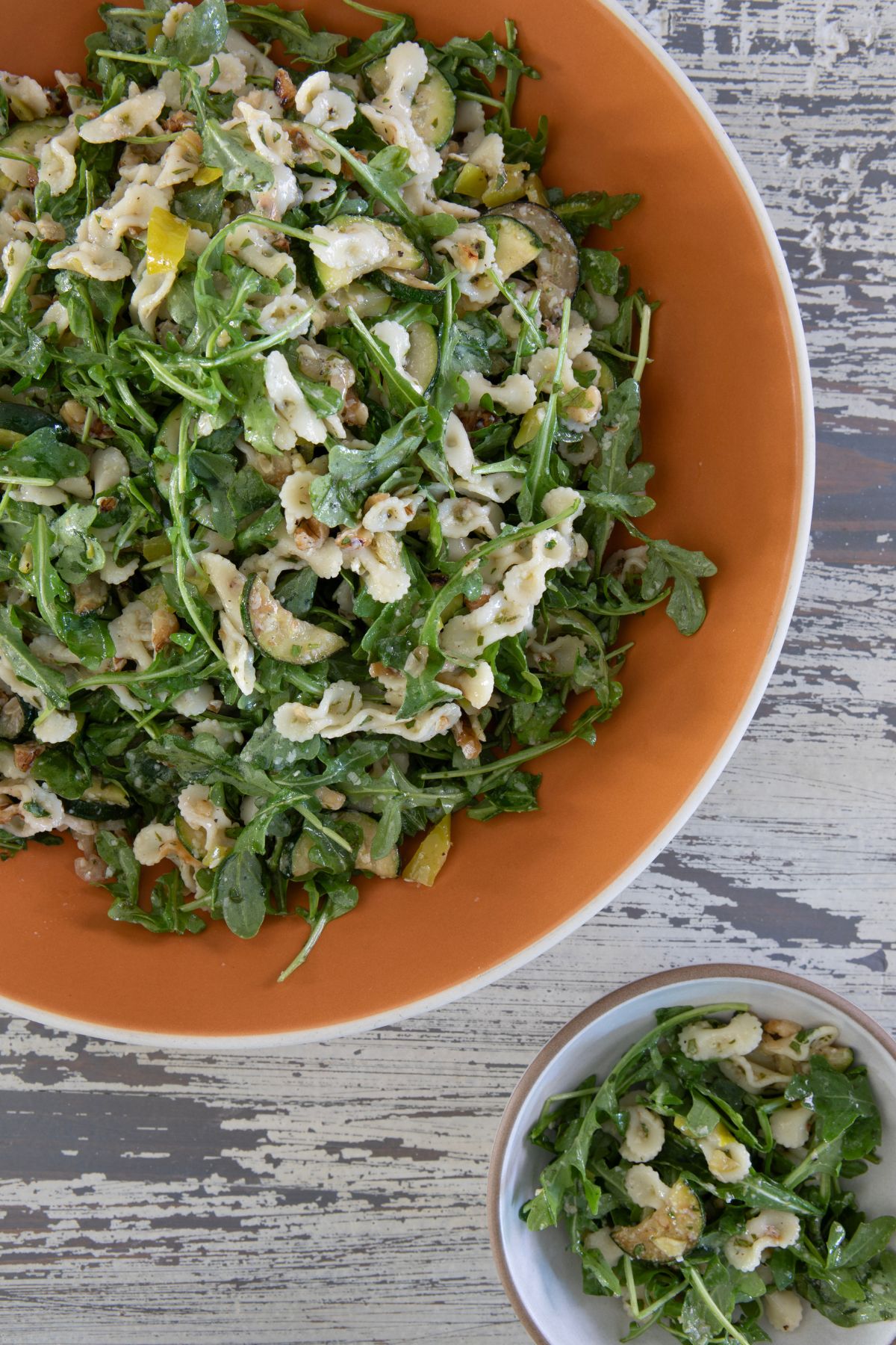 Overhead view of arugula pasta salad with zucchini and pepperoncini dressing served in white bowl