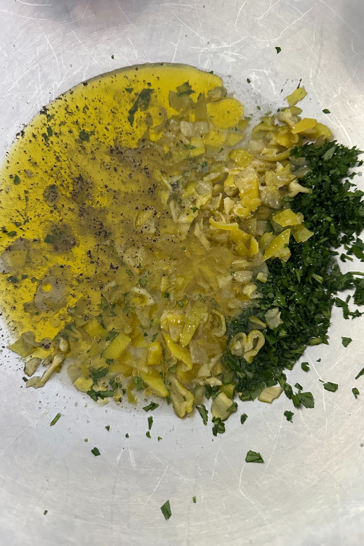Whisking pepperoncini vinaigrette in bowl with herbs and garlic