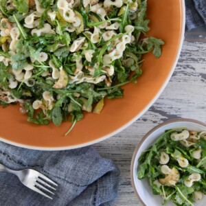 Bowl of arugula pasta salad with zucchini, walnuts, and pepperoncini dressing