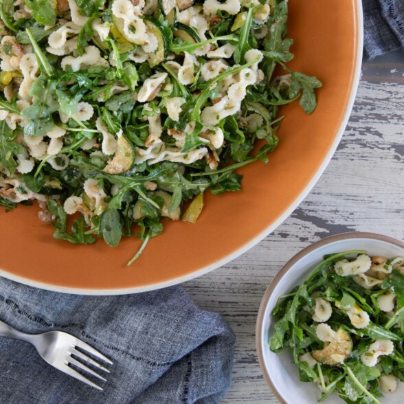 Bowl of arugula pasta salad with zucchini, walnuts, and pepperoncini dressing