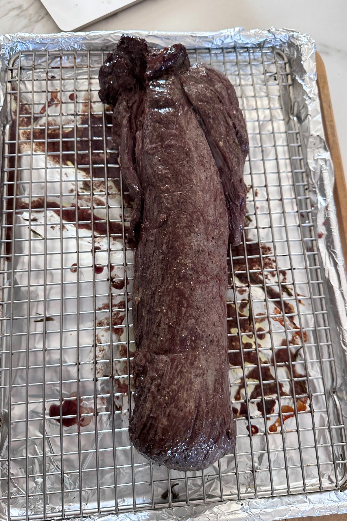 Beef tenderloin resting on a cooling rack set over a foil-lined baking sheet with the twine removed.