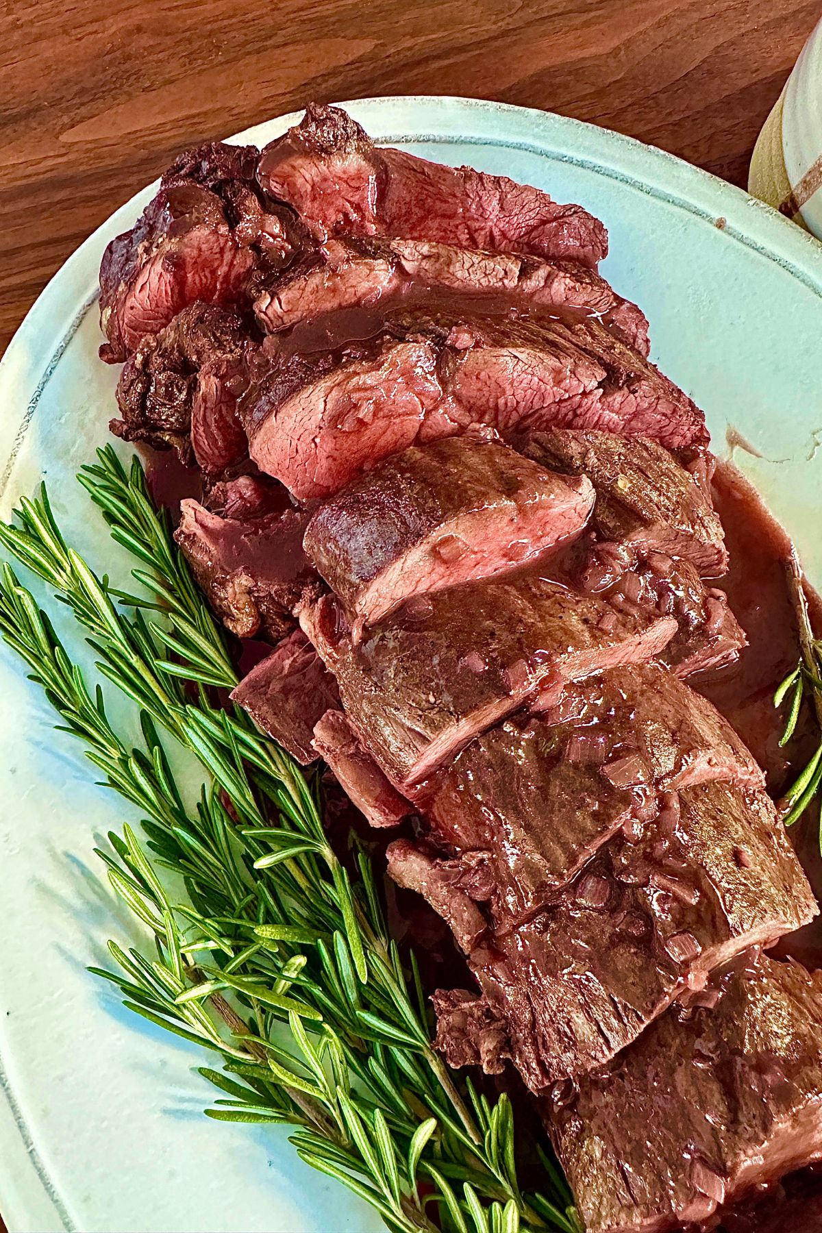 Beef tenderloin sliced into rounds and plated with rosemary sprigs and red wine sauce surrounding it.