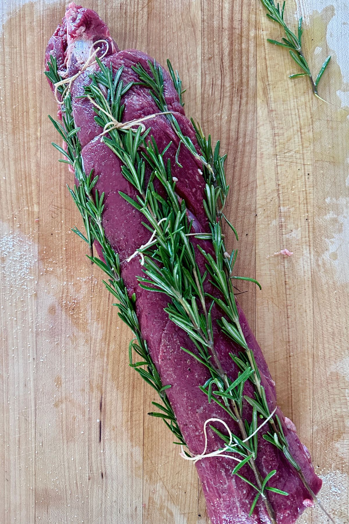 Beef tenderloin rubbed with olive oil, generously seasoned, and tied with twine every two inches with rosemary sprigs tucked under the twine.