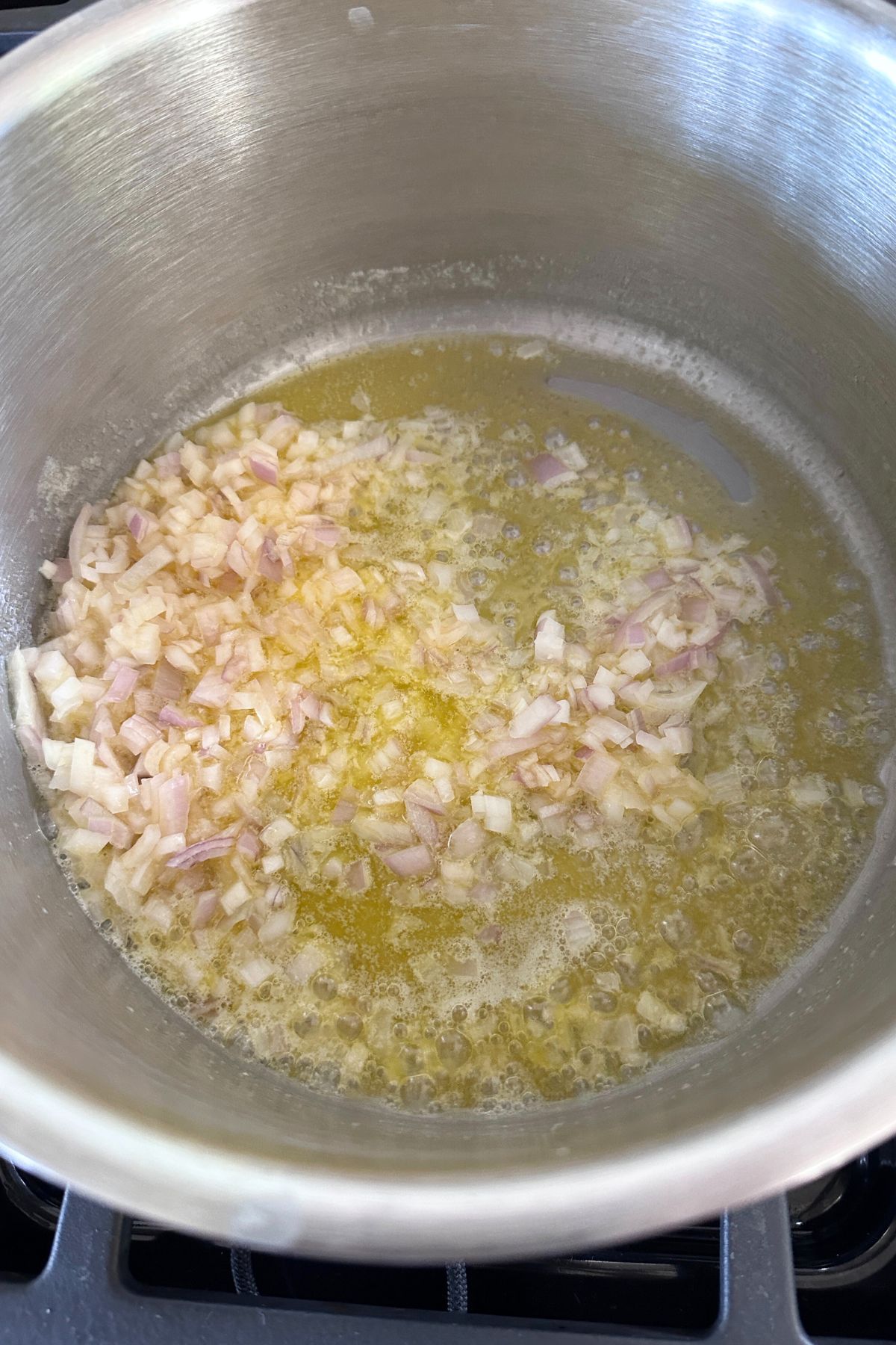 Chopped shallots cooking in butter, wine, and broth in a large pot.