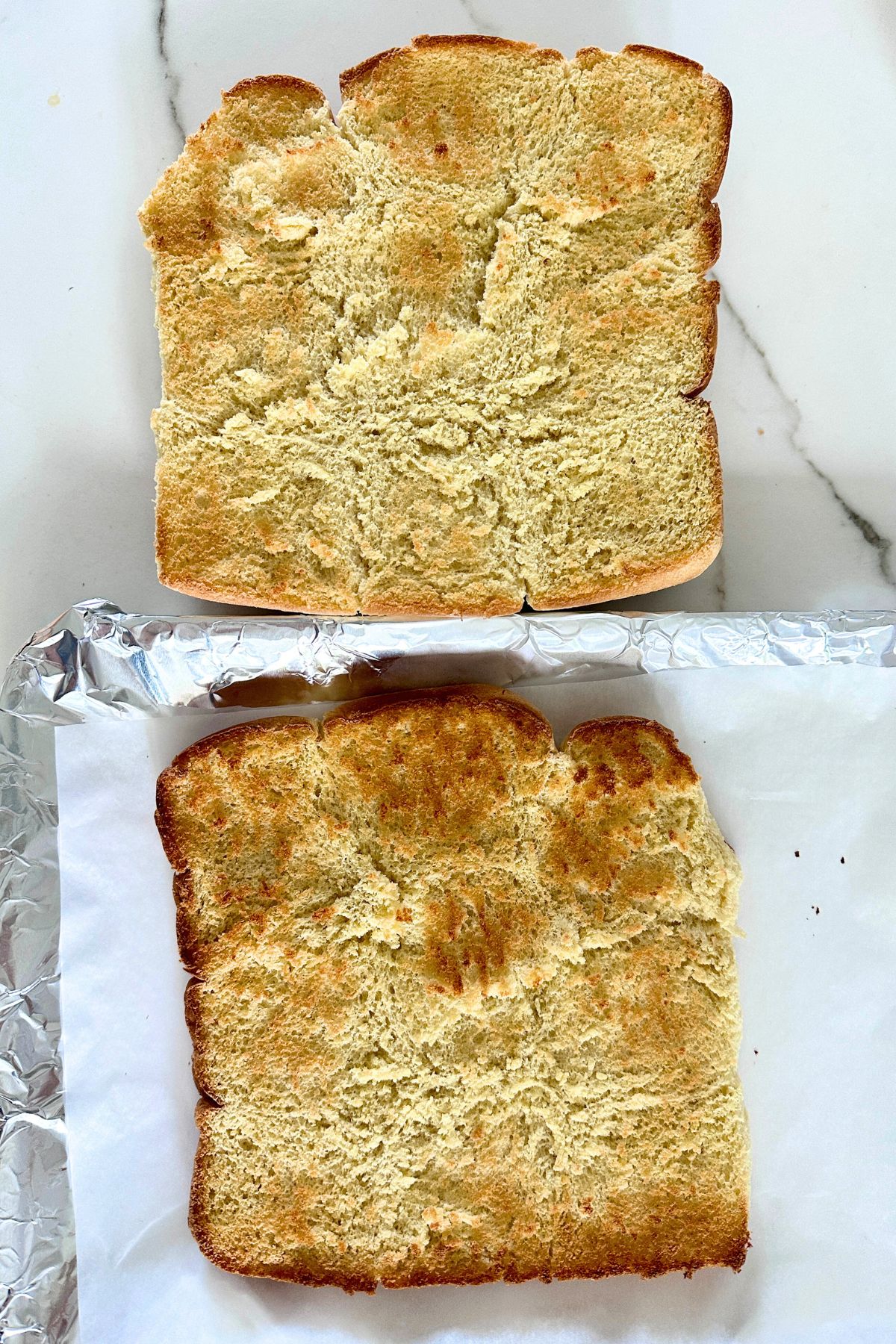 Toasted slider buns split and arranged cut side up on a foil-lined baking sheet.