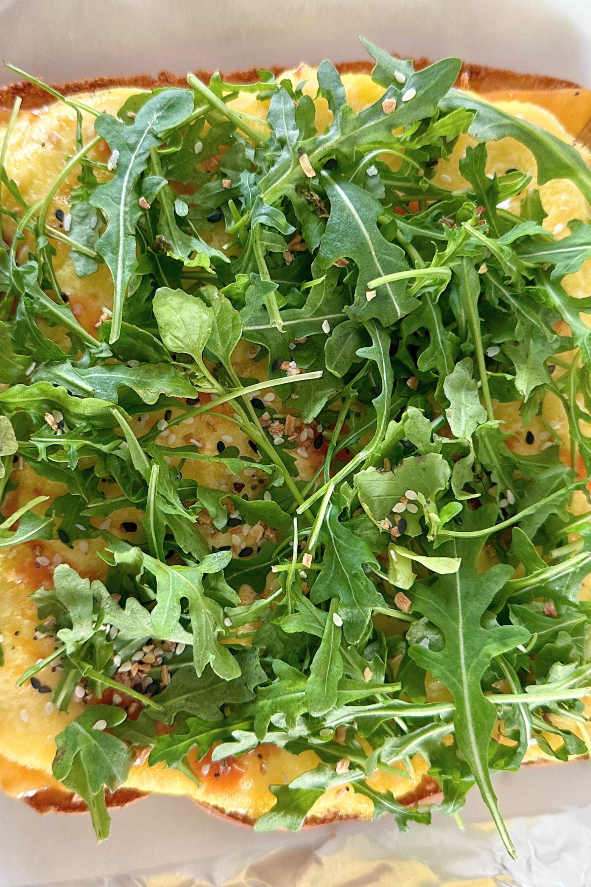 Arugula, seasoning, melted cheese, and a sliced baked egg layer stacked on toasted slider buns.