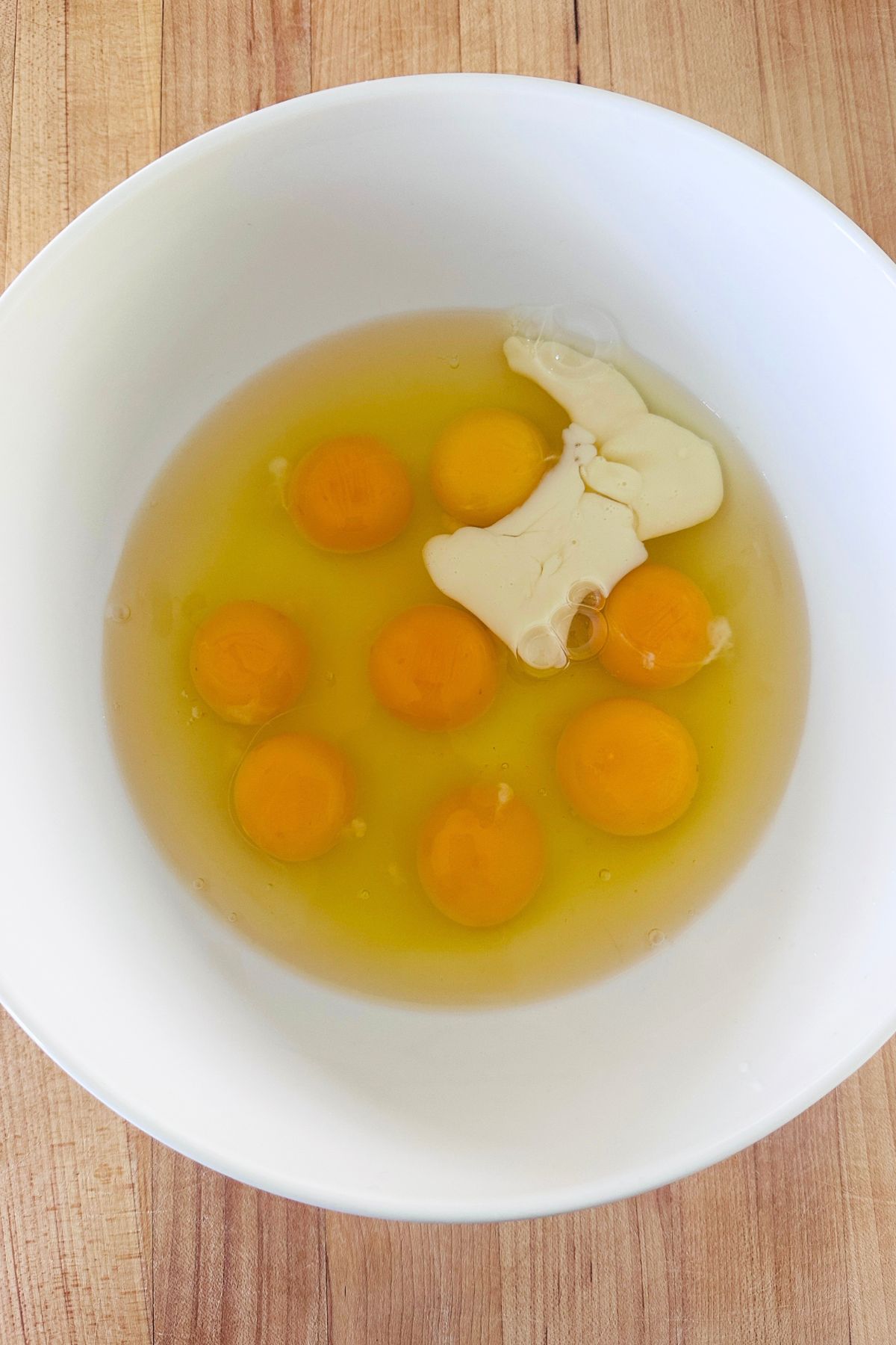 A white glass mixing bowl with eggs, milk, and salt.