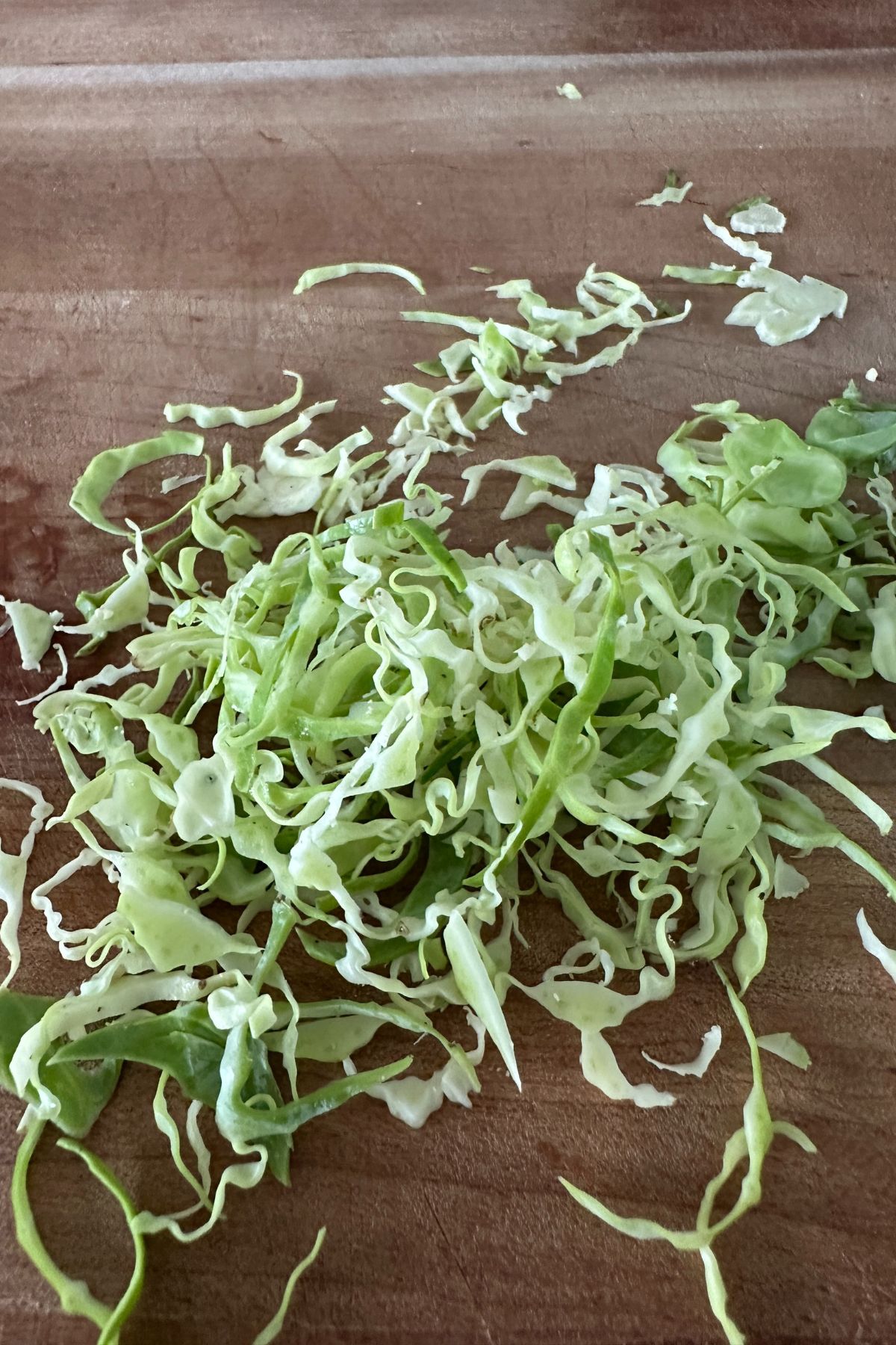 Thinly sliced brussels sprouts on a wooden cutting board.