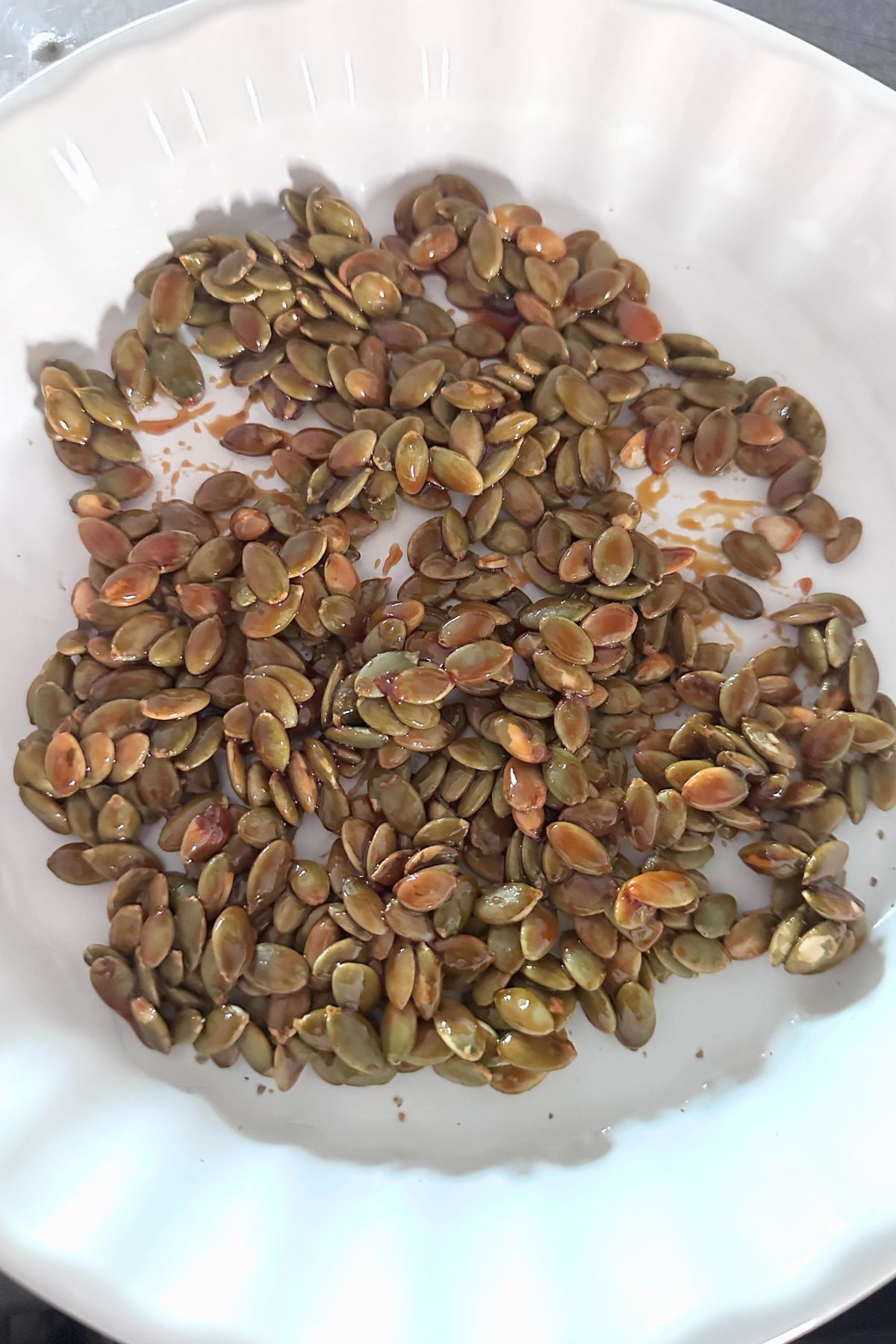 Candied pumpkin seeds cooling in a white glass bowl.