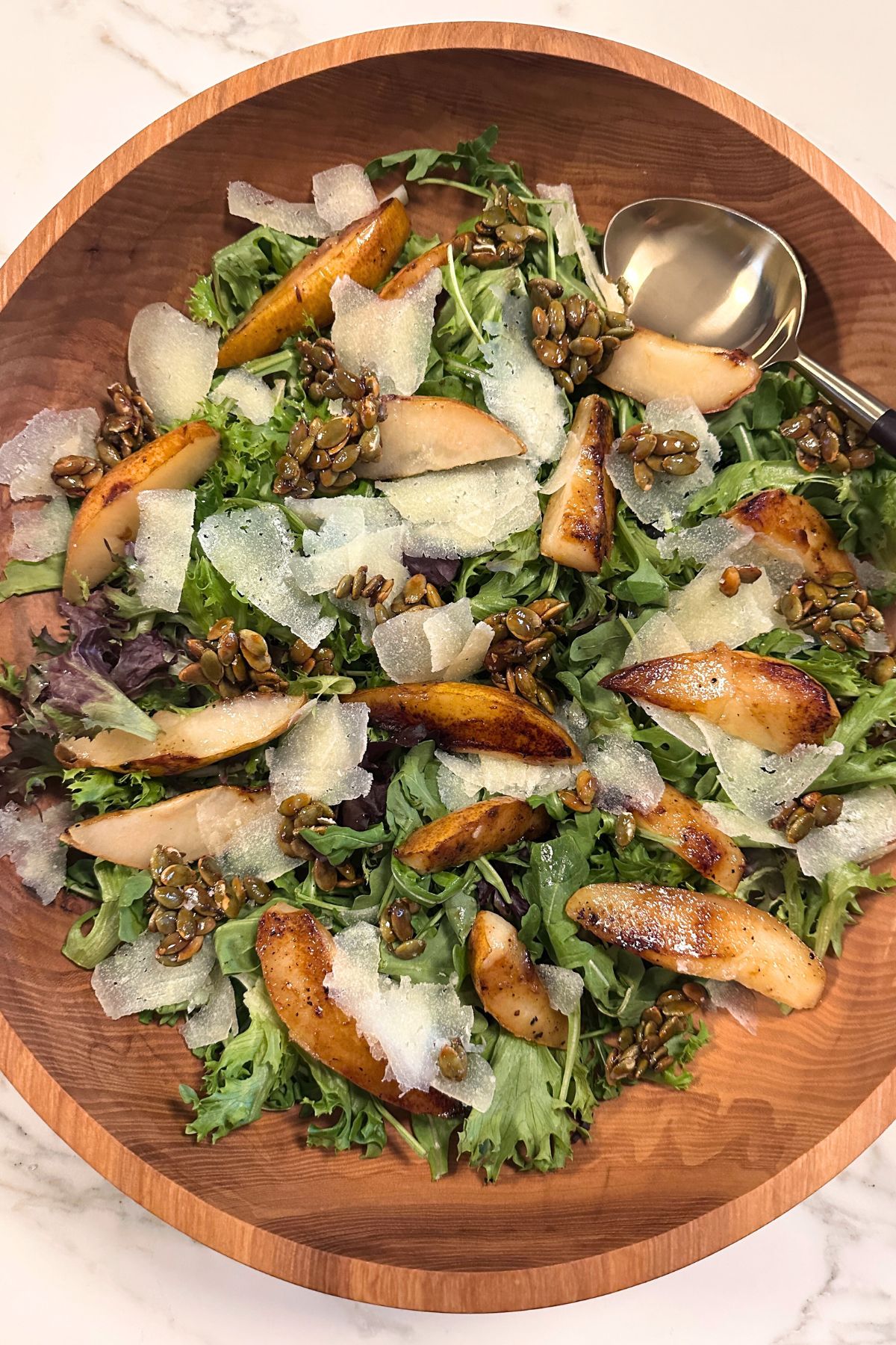 Close-up of caramelized pear salad with crisp greens, blue cheese, and crunchy candied pumpkin seeds.