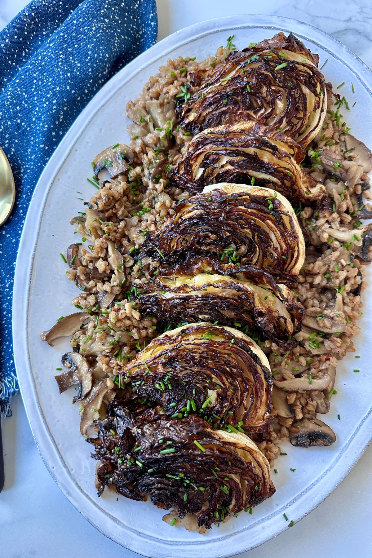 Mushroom farro on a white serving platter topped with charred cabbage wedges. 