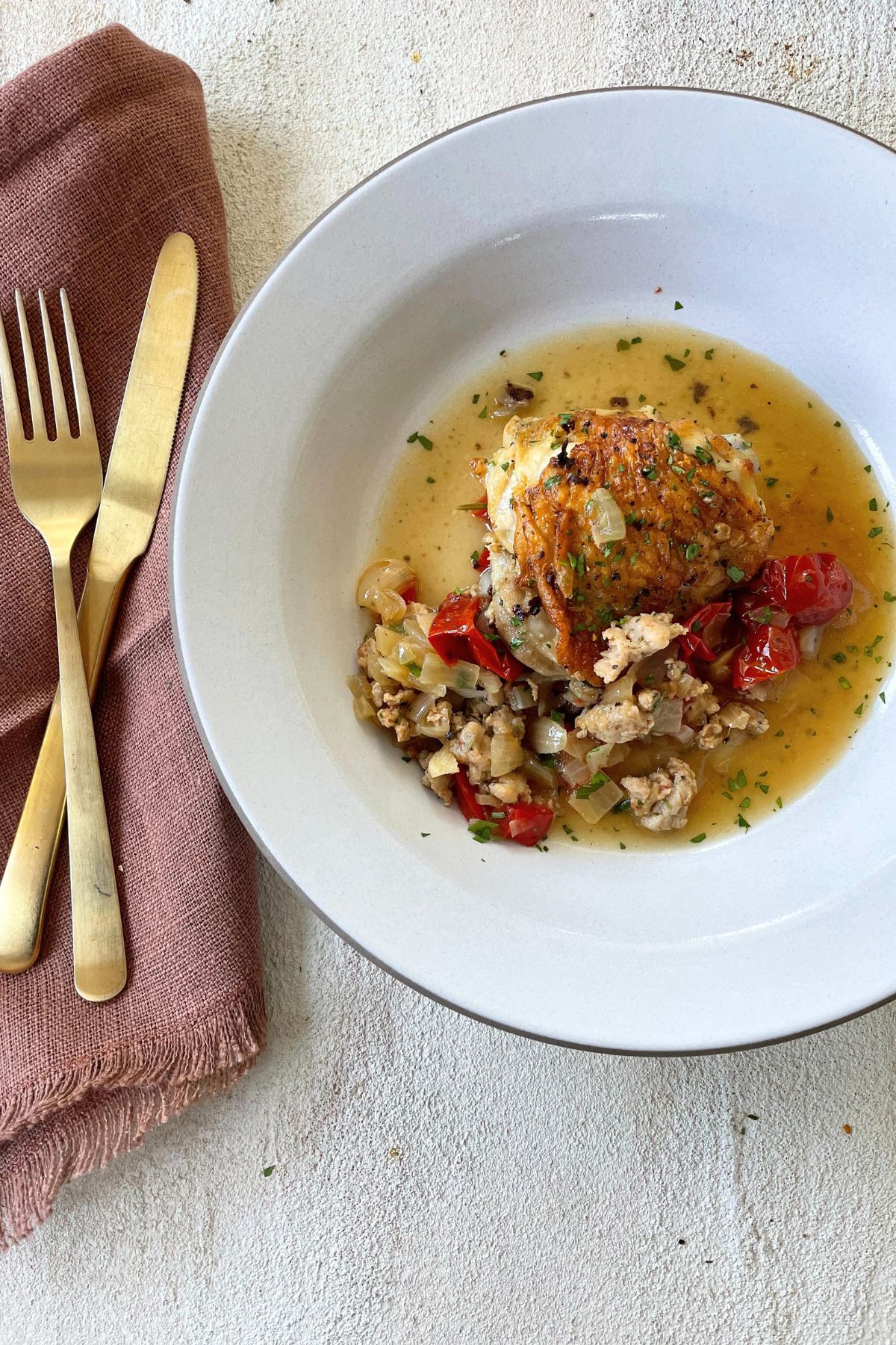 Finished chicken scarpariello served in a white bowl with a golden fork and knife beside it, ready to eat.