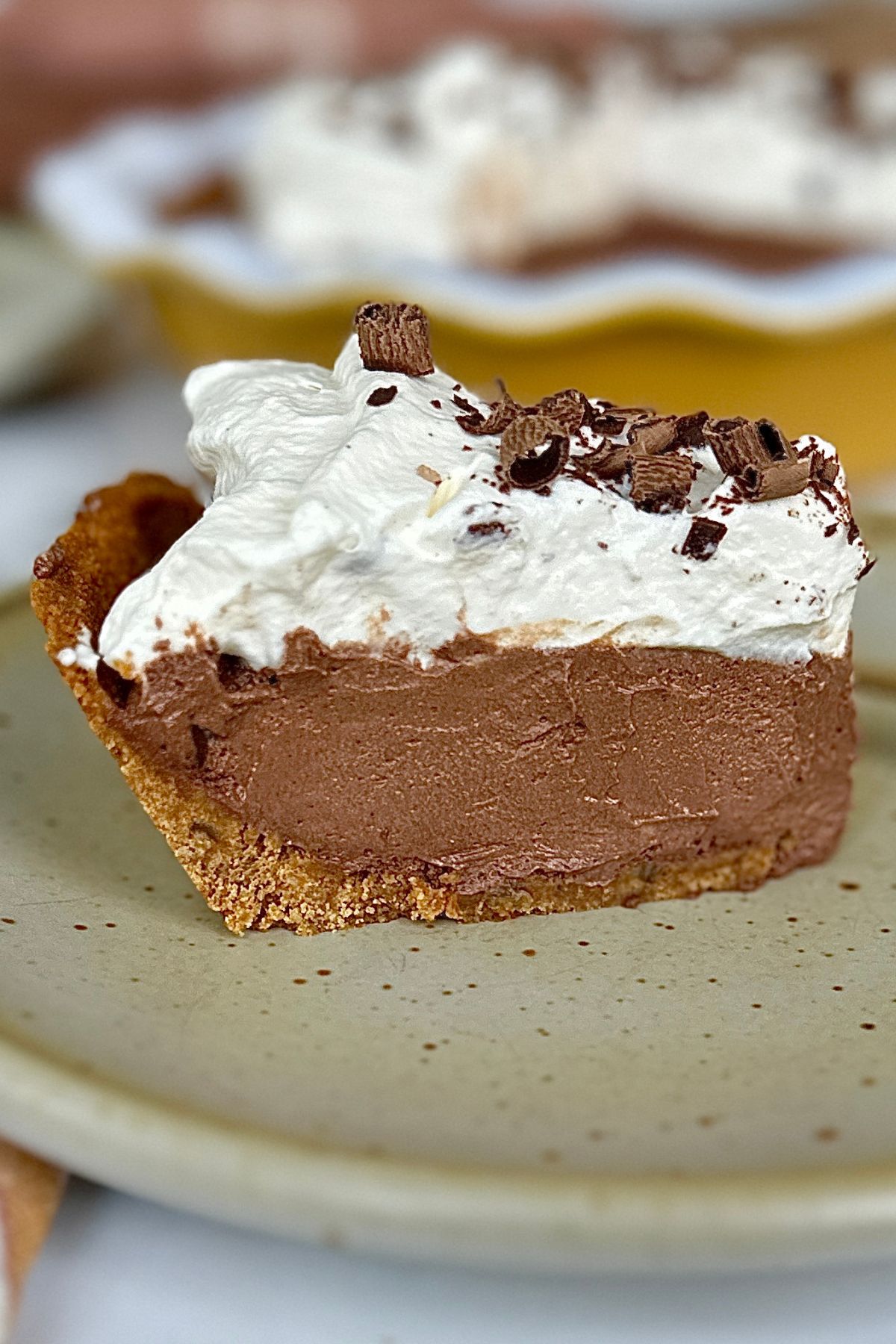 Side view of a slice of gingersnap pie crust with chocolate fillin; garnished with whipped cream and chocolate shavings.