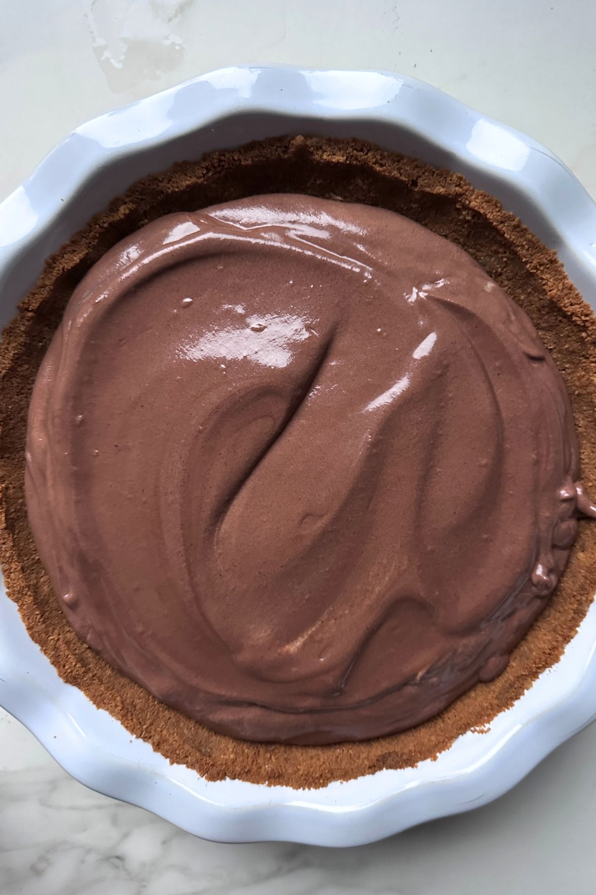 Chocolate pie filling spread evenly into prepared pie crust, ready to refrigerate.