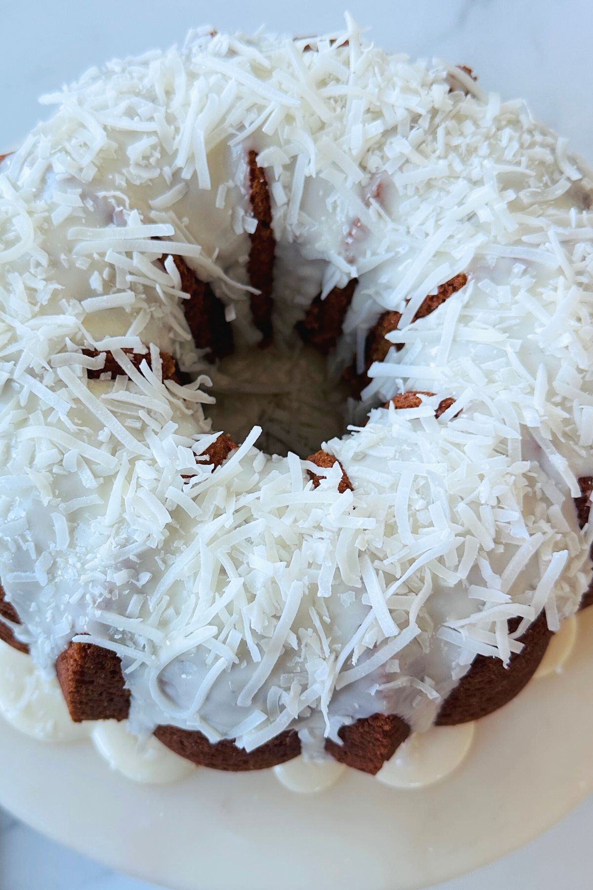 Coconut bundt cake frosted with a glaze and topped with shredded coconut flakes.
