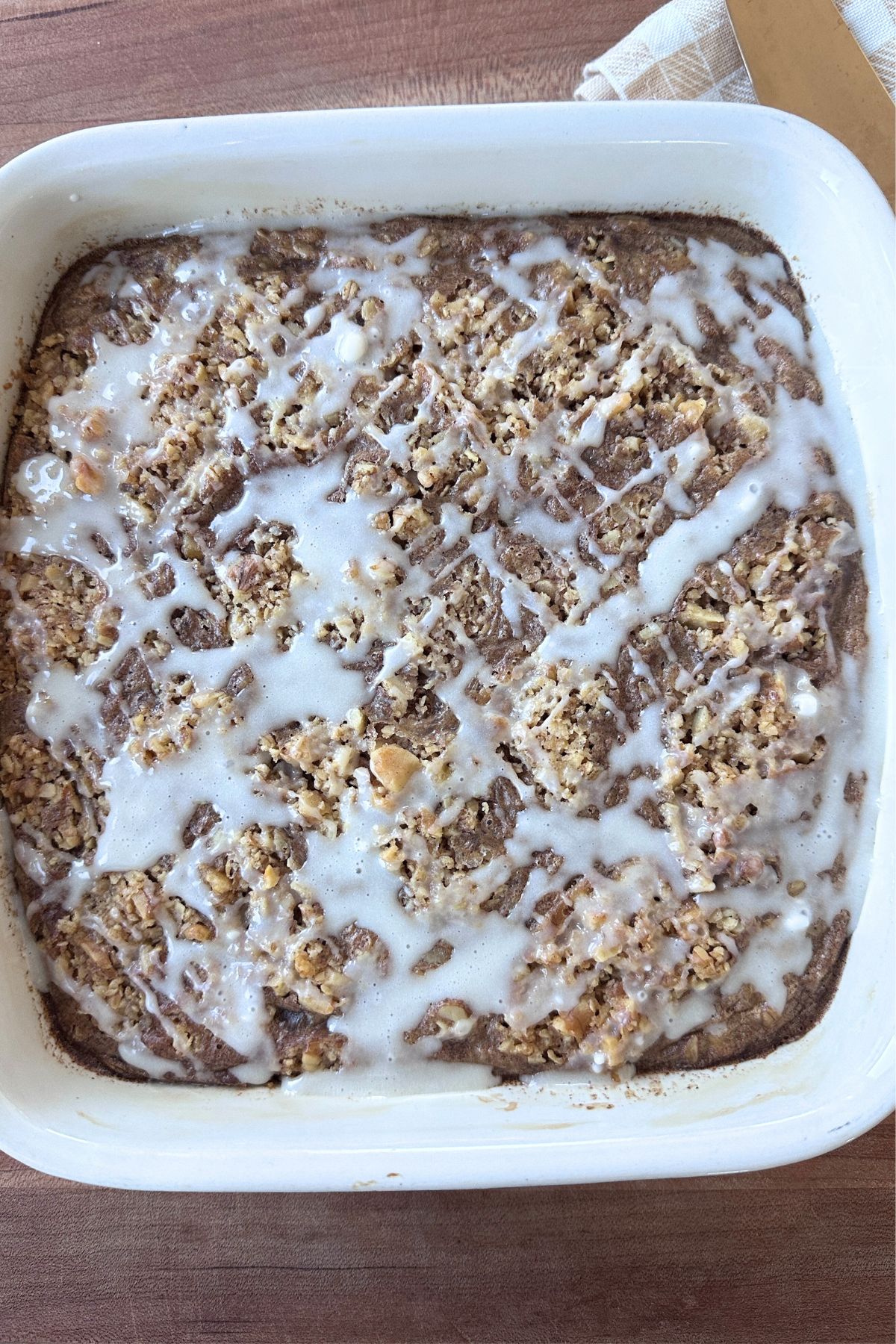 Coffee cake baked oatmeal drizzled with glaze in a square white baking dish.