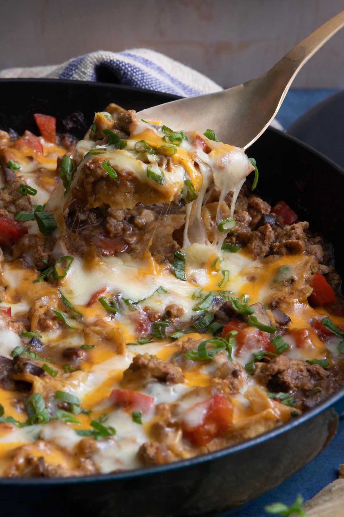 Green chile enchiladas in a skillet topped with melted cheese, cilantro, and green onions, ready to serve.