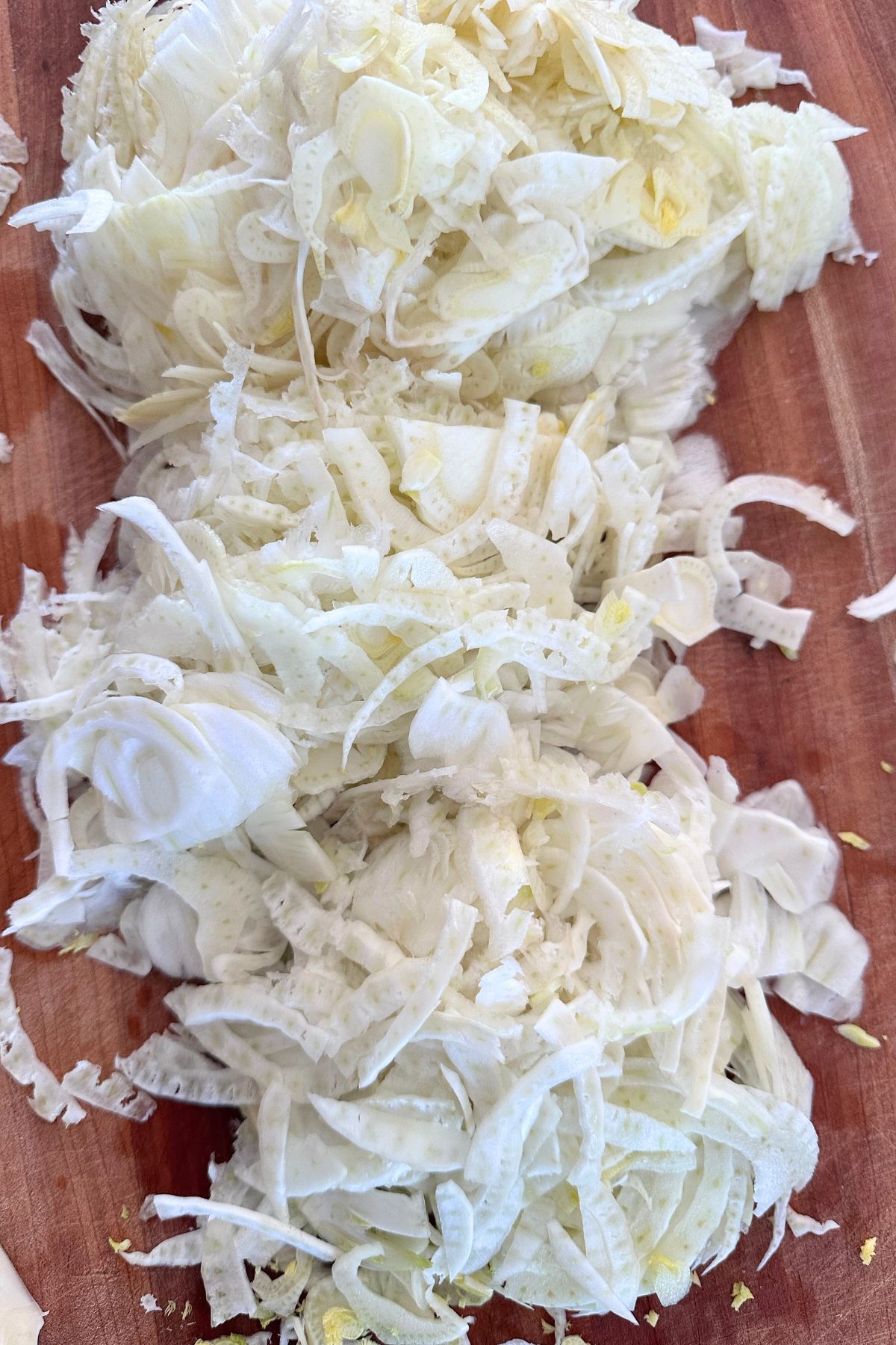 Thinly sliced fennel stems and chopped fennel fronds on a wooden cutting board.