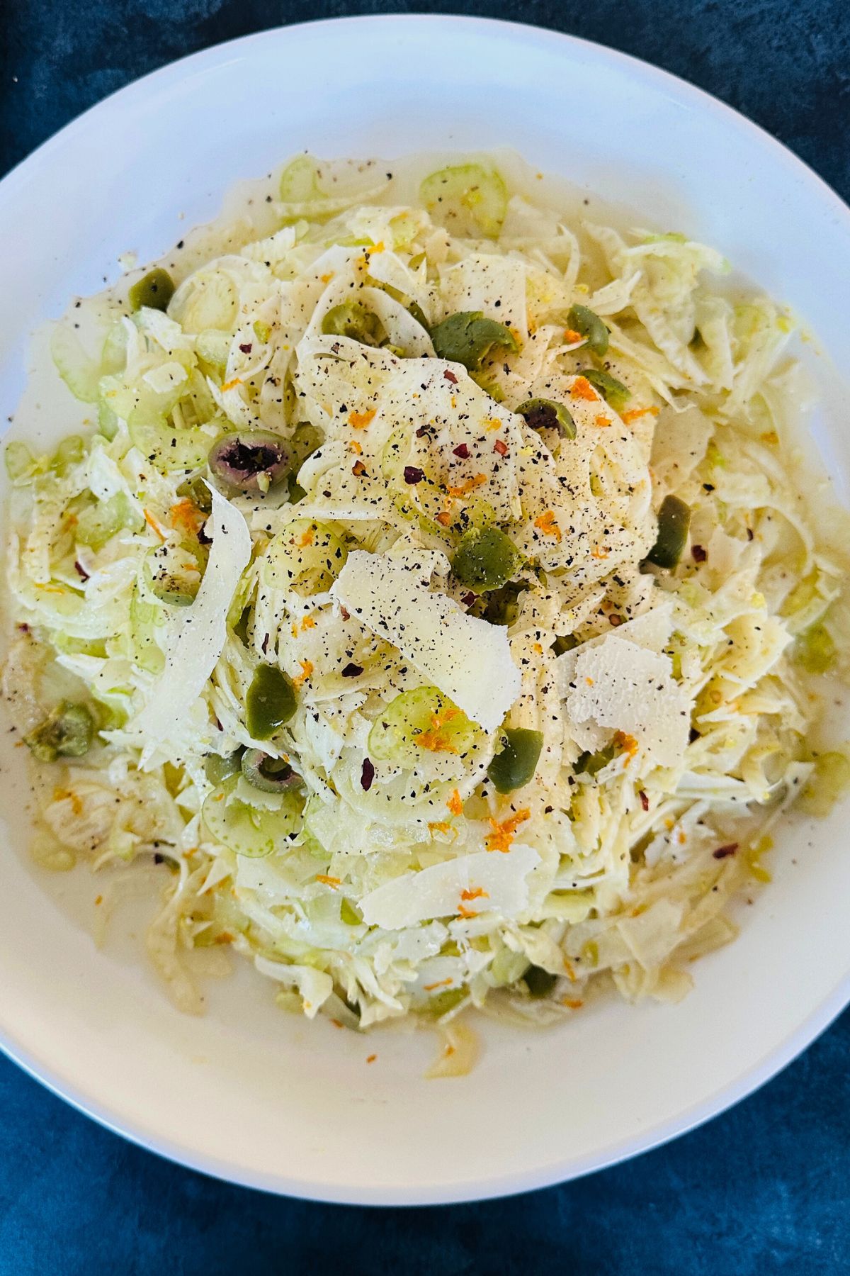 Dressed, shaved fennel over a mixture of fennel stems and olives, topped with shaved Parmesan in a bowl.