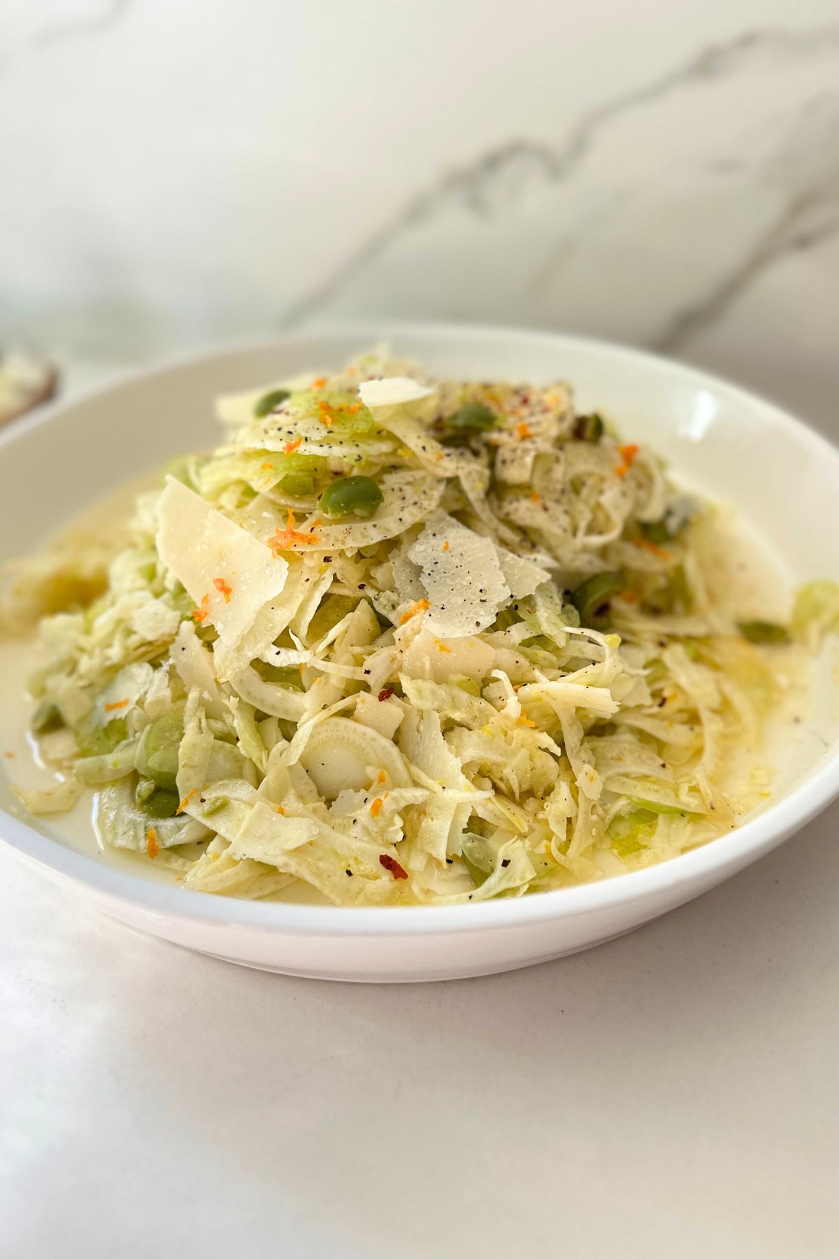 Fennel salad recipe in a white bowl garnished with freshly shaved parmesan.