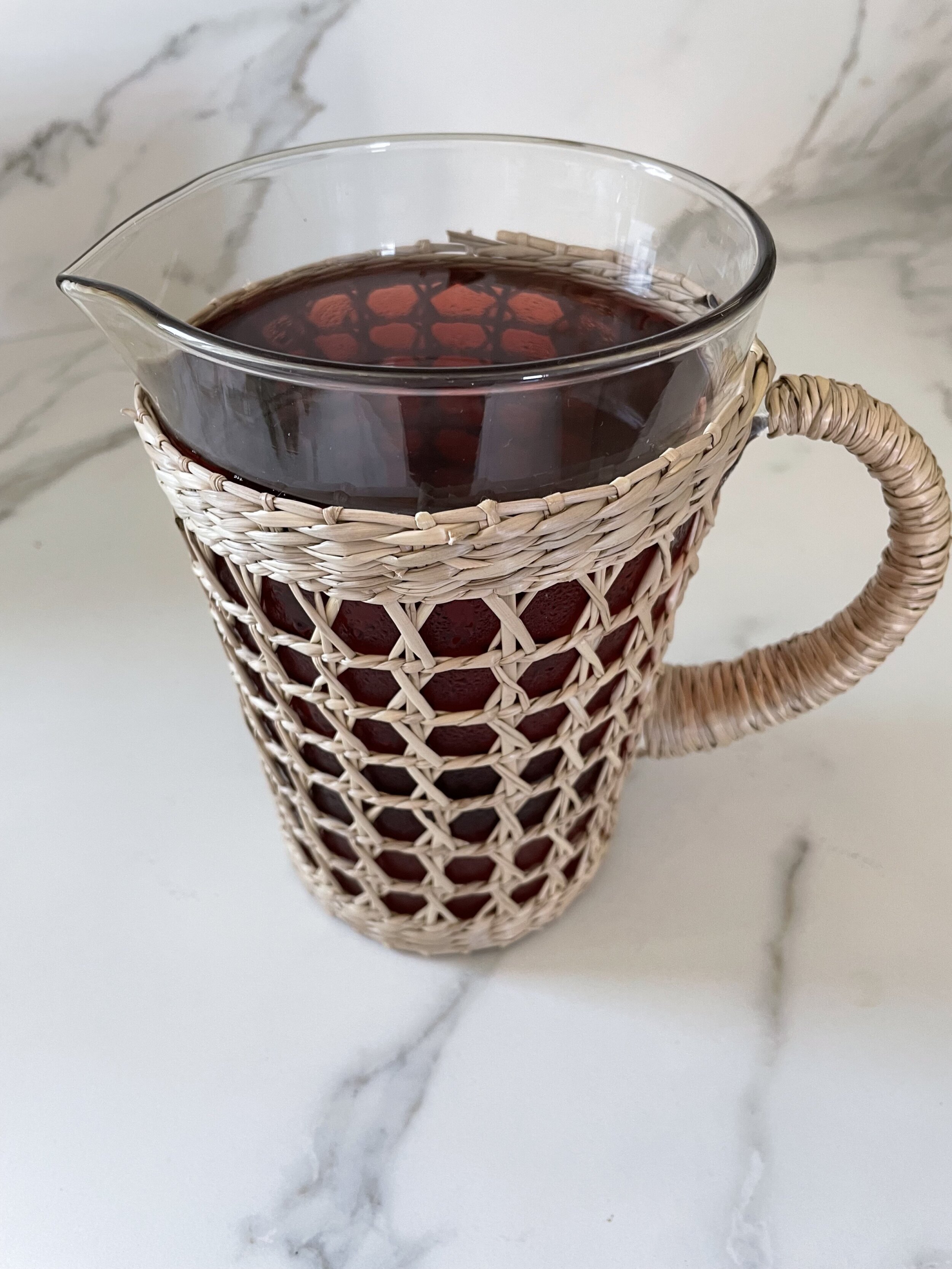 A large glass pitcher of hibiscus mocktail on a light colored countertop.
