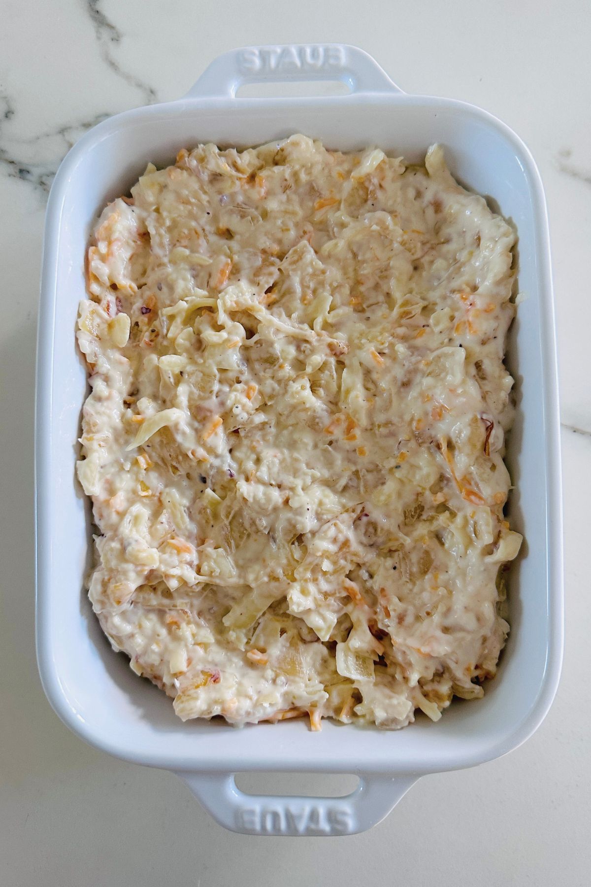 Onion dip in a large white oven-safe baking dish; ready to bake.