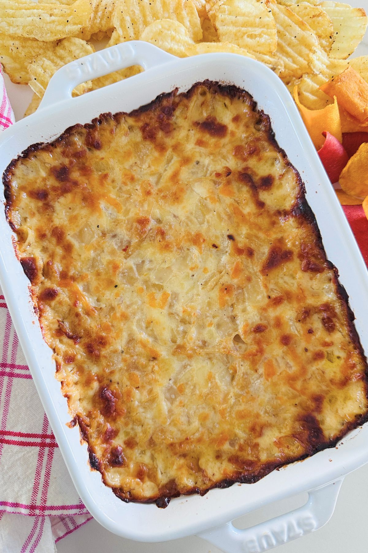 Hot onion dip in a large white baking dish surrounded by potato chips.