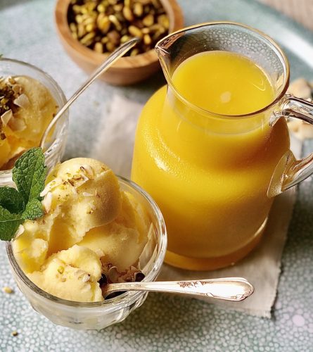 a serving of orange sherbet in a small glass with a spoon 