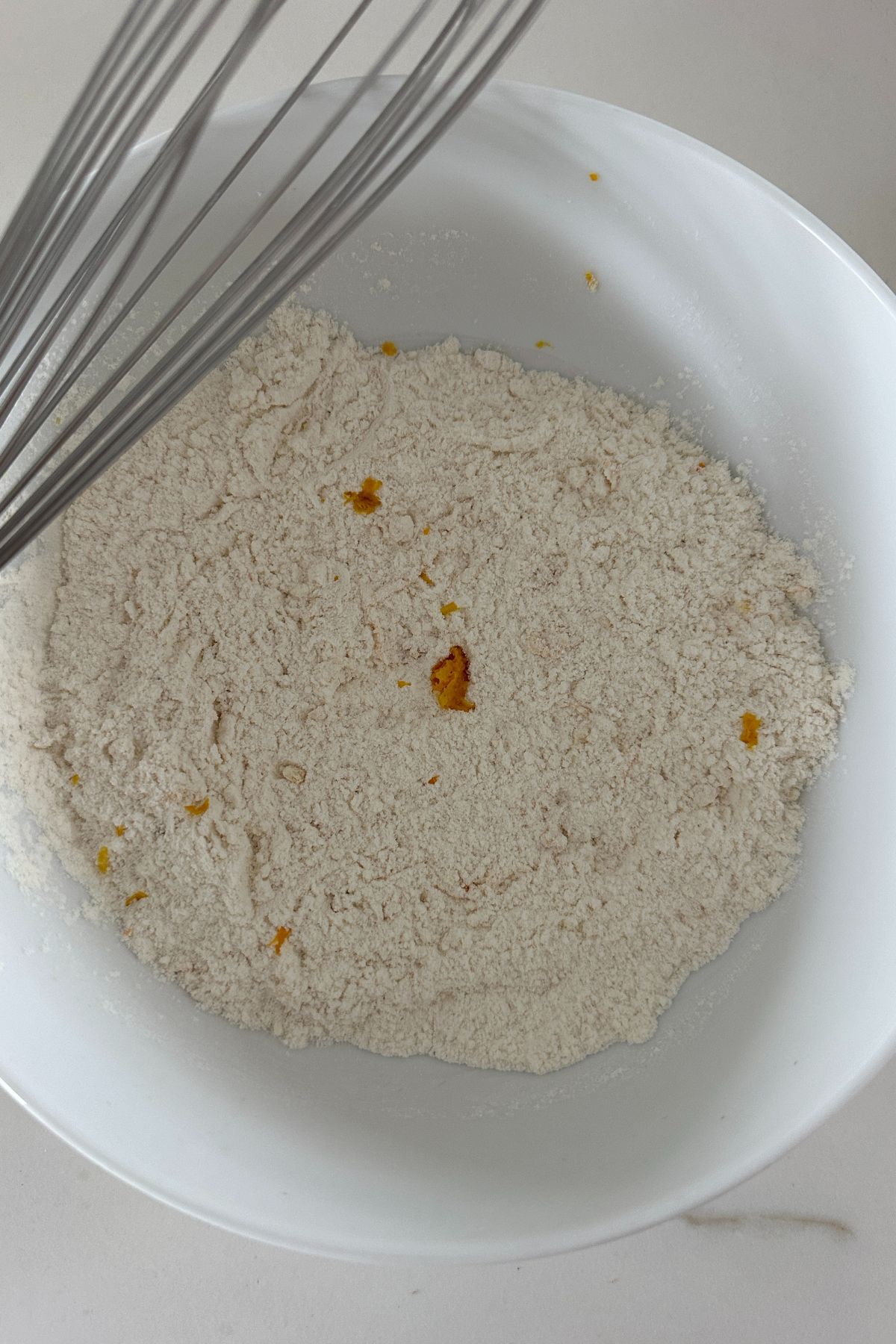 White mixing bowl with dry ingredients including flour, baking powder, orange zest, salt, and nutmeg for invisible apple cake.