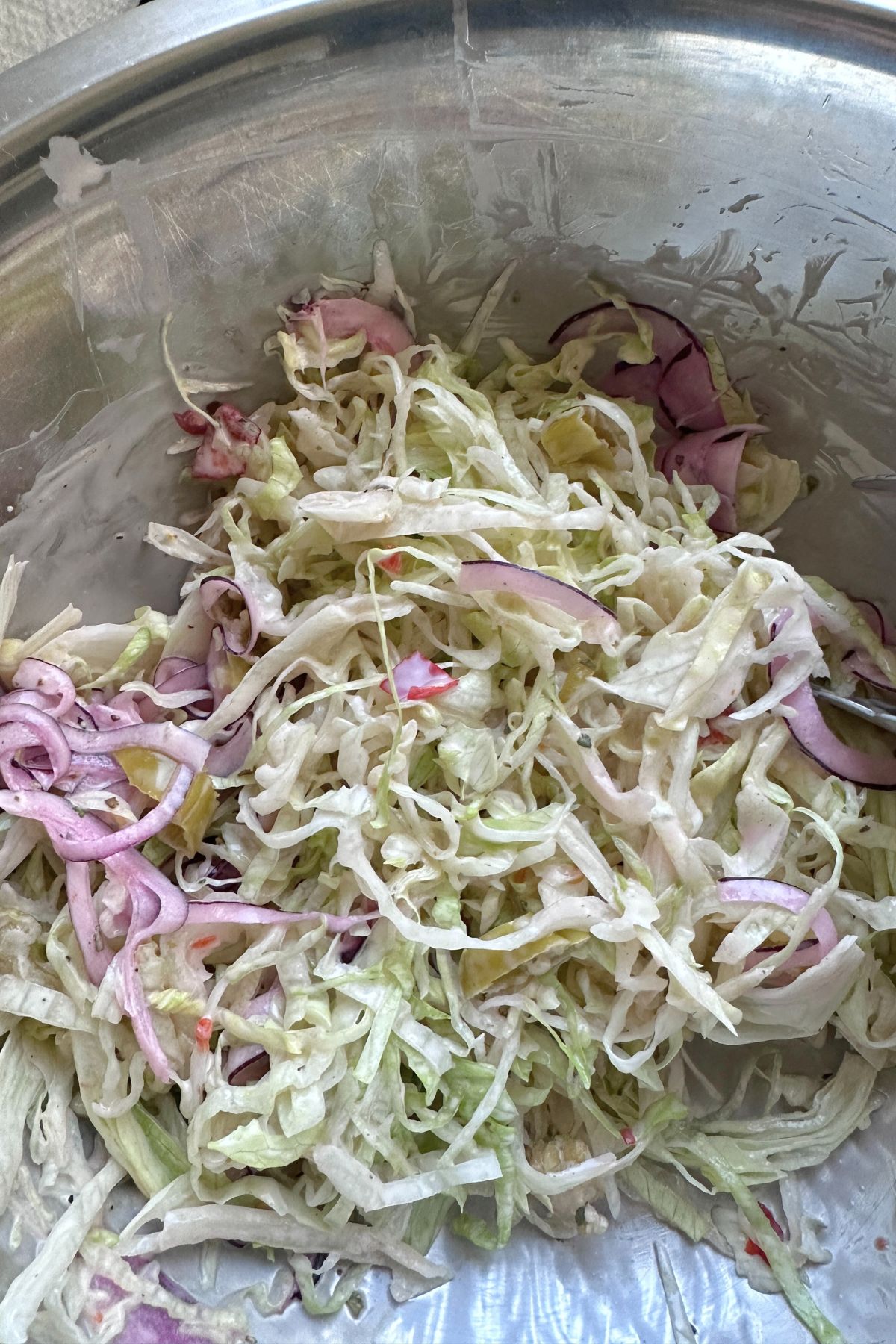 Lettuce, red onion, and pepperoncini in a bowl tossed in dressing.