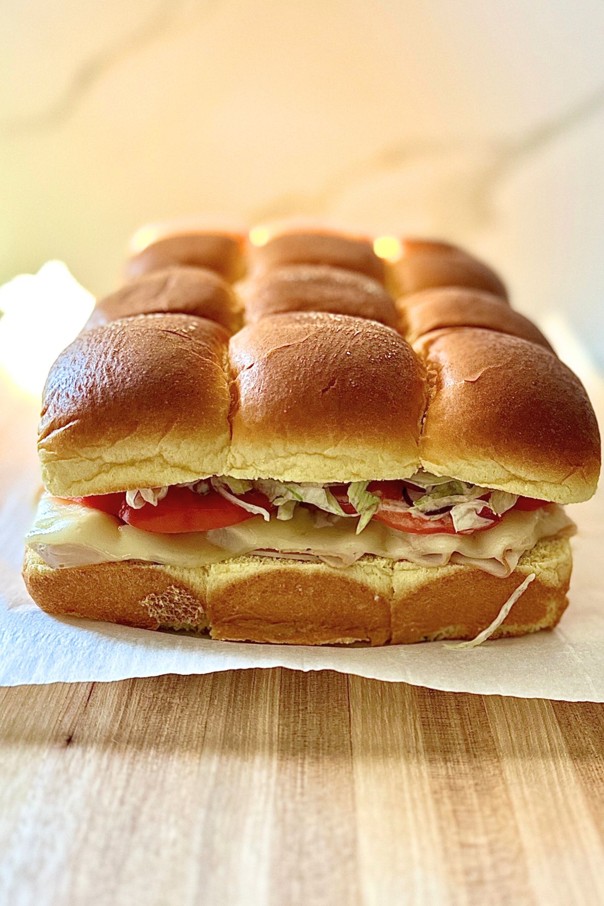 Side view of Italian grinder sliders on parchment paper on a wooden cutting board.