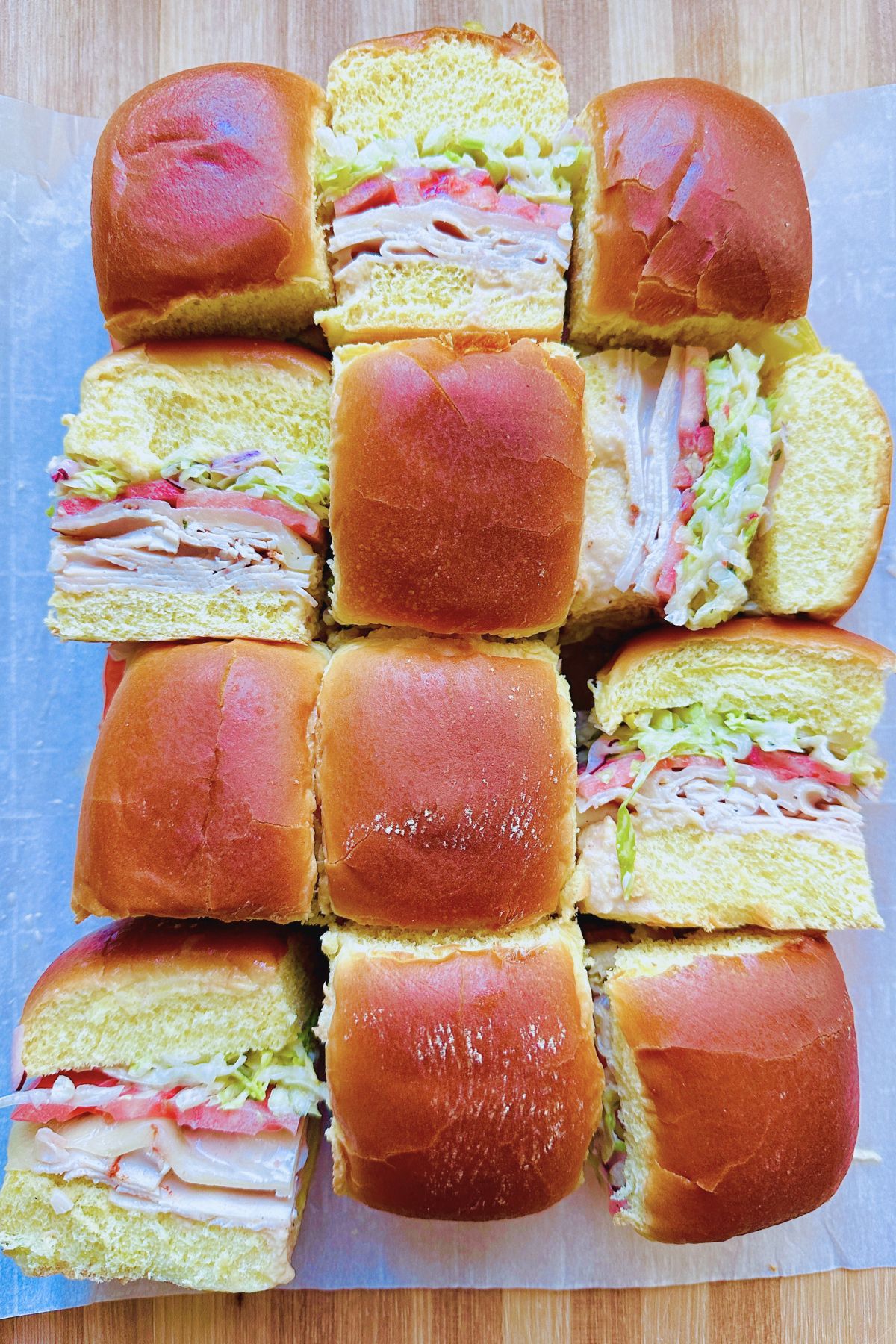 Italian grinder sliders arranged on a baking sheet, with some upright and others flipped to show the layered filling inside.