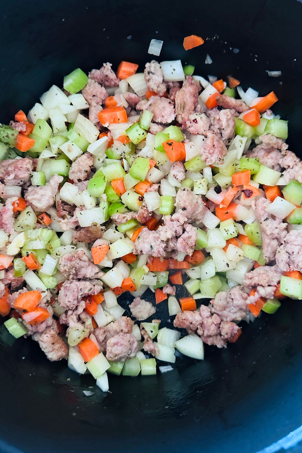 Italian sausage browning in a large pot with onion, carrots, celery, garlic, and seasonings.