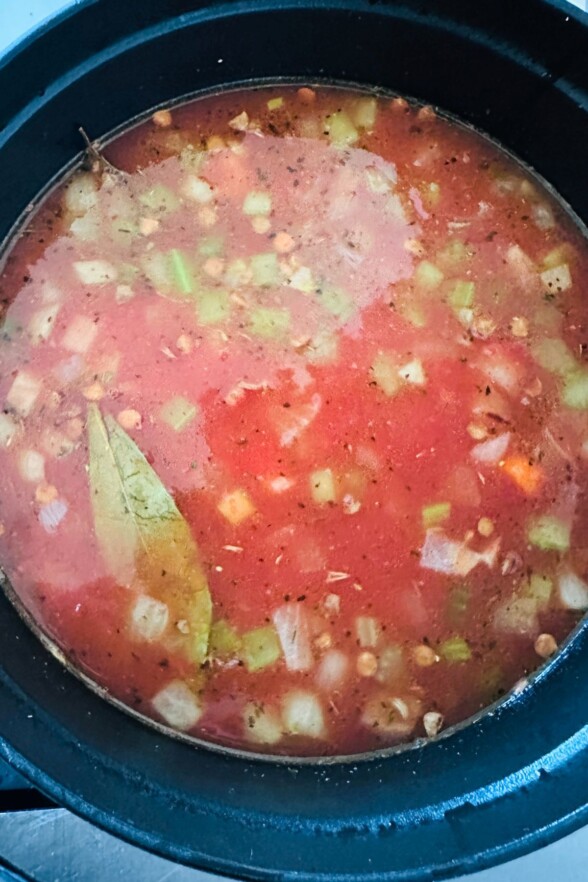 Lentil soup simmering in a pot with sausage, tomatoes, bay leaves, and vegetables.