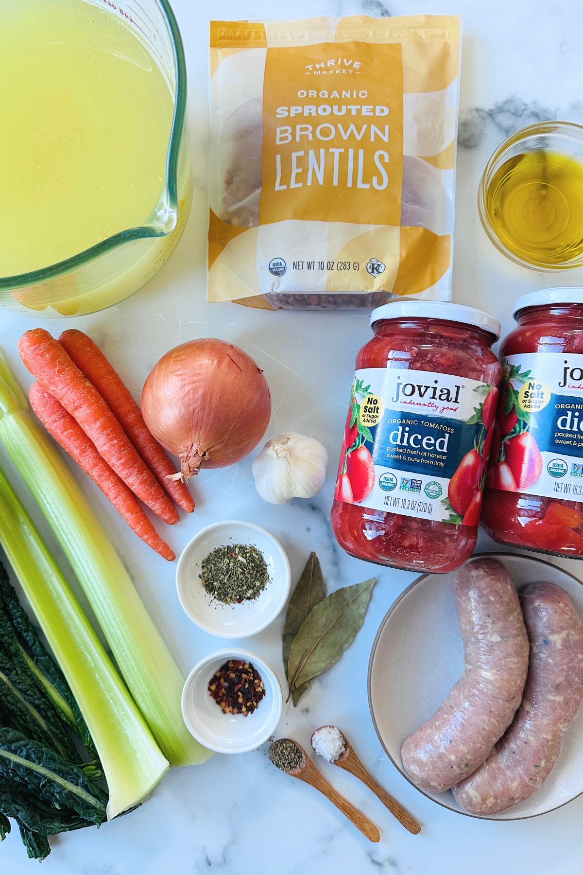 Ingredients for sausage lentil soup laid out on a white countertop.