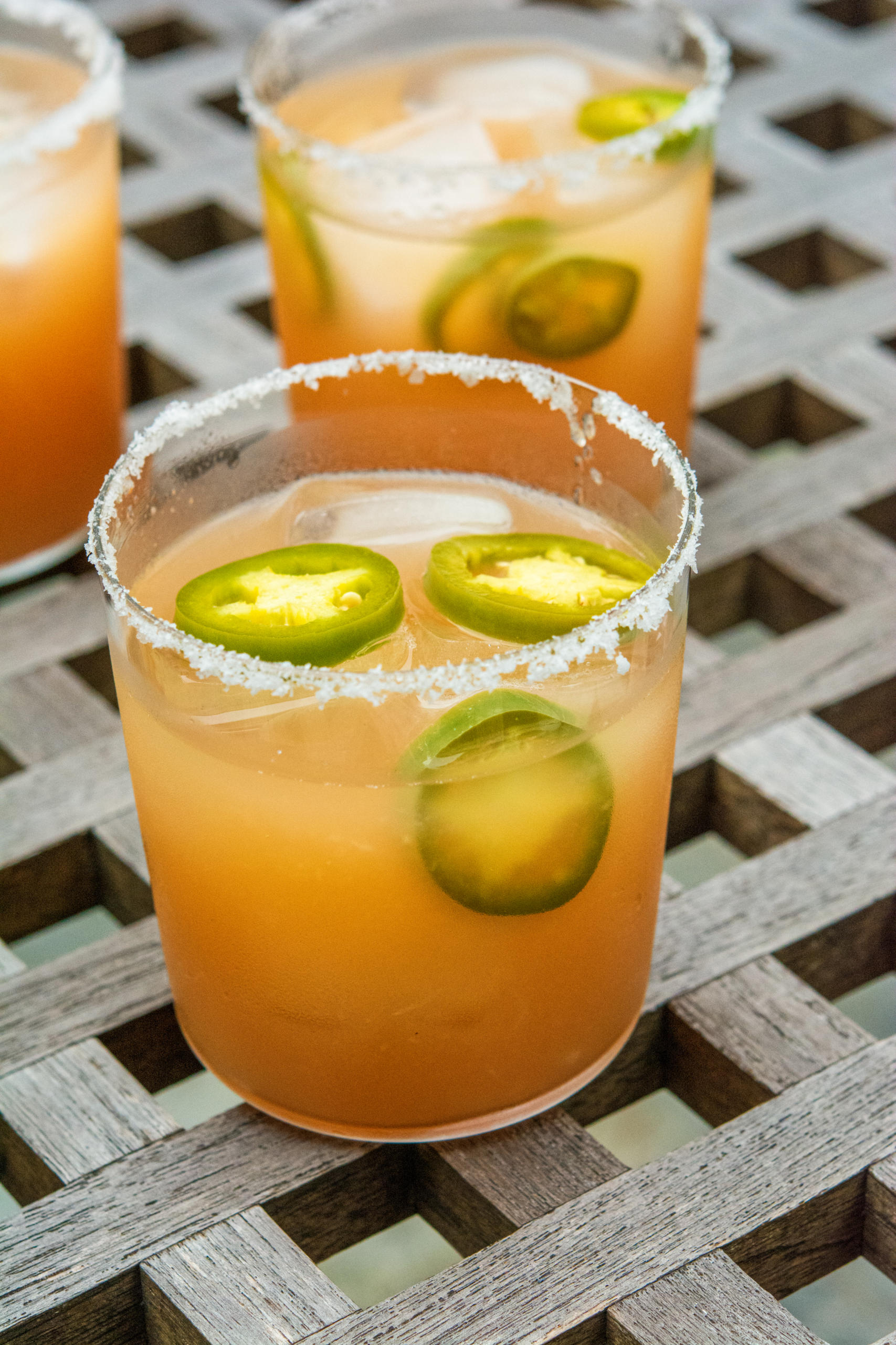 A close-up of a spicy margarita with sliced jalapenos and chili salt rim on glass.