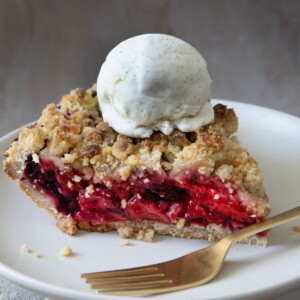 A slice of freshly baked mixed berry crumble pie with jewel-toned berries and golden streusel topping with a scoop of vanilla ice cream