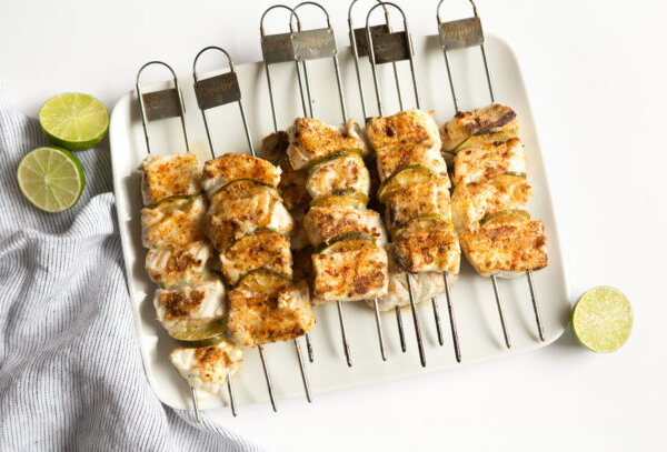 Raw halibut skewers with lime slices ready for grilling, arranged on a white cutting board.