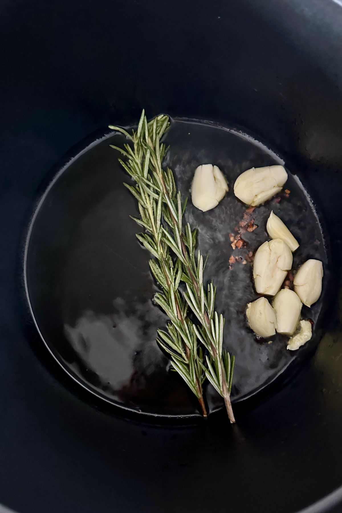 Garlic, rosemary, and red pepper flakes sizzling in olive oil in a pot for Pasta e Ceci.