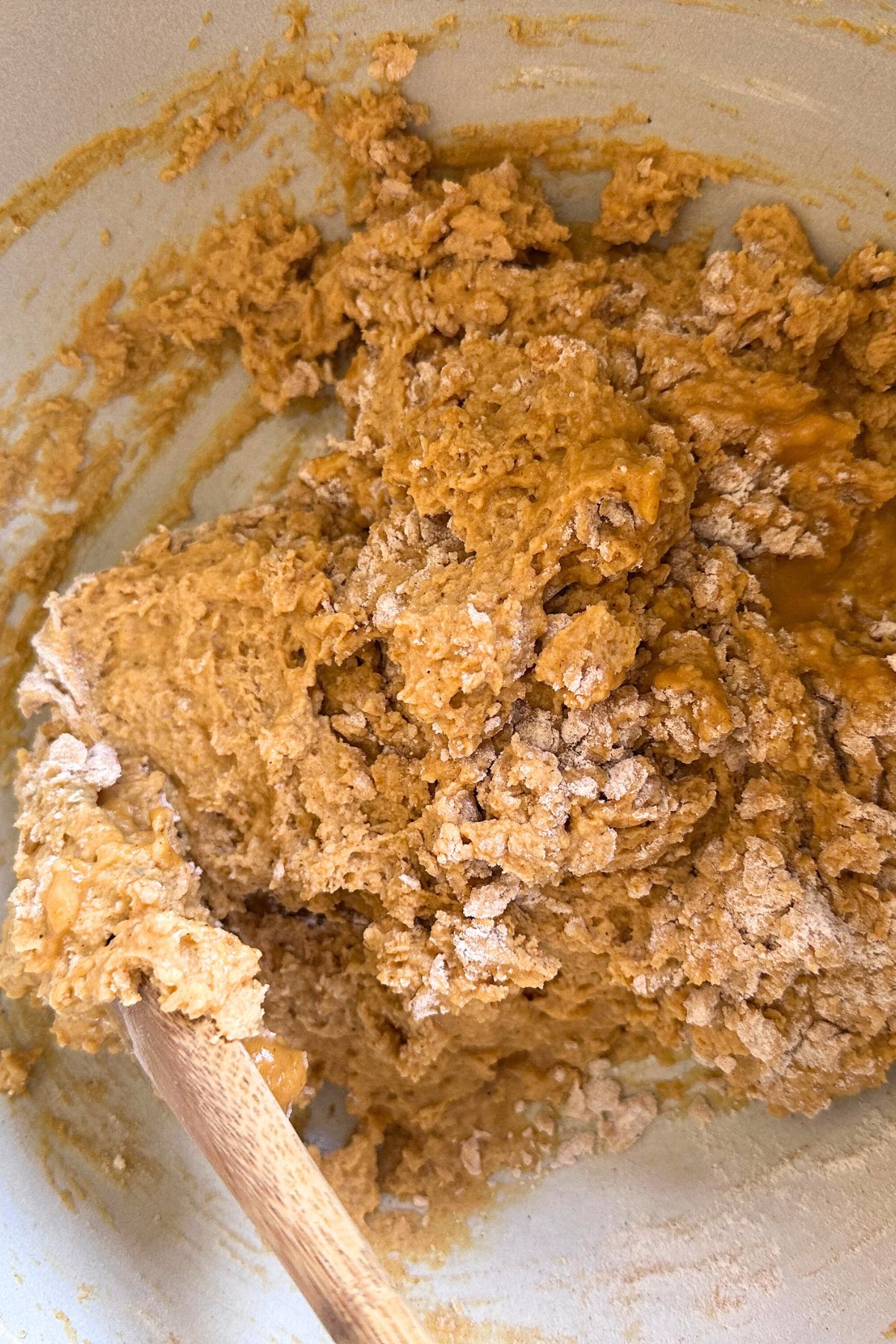 A wooden spoon folding the dry ingredients into the wet mixture, forming a thick batter.