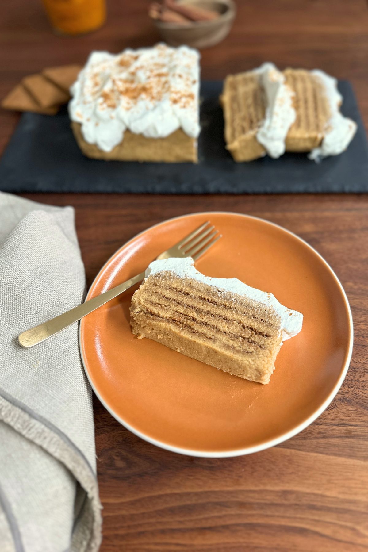 A slice of pumpkin icebox cake topped with whipped cream on an orange plate, ready to eat.