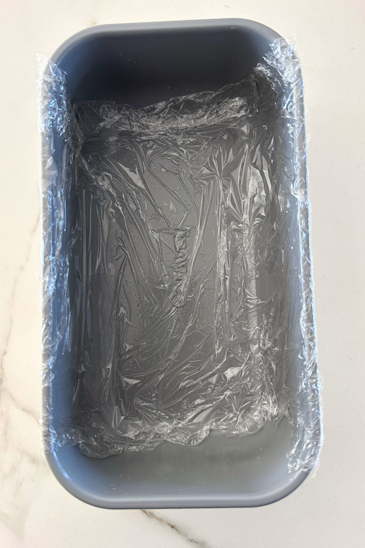 Plastic wrap lined loaf pan on a white counter top.