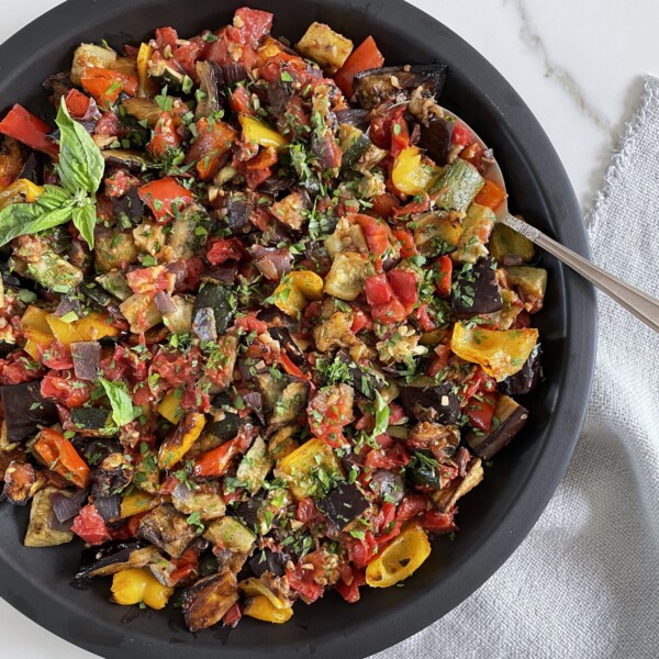 Bowl of roasted ratatouille with colorful summer vegetables and fresh herbs.