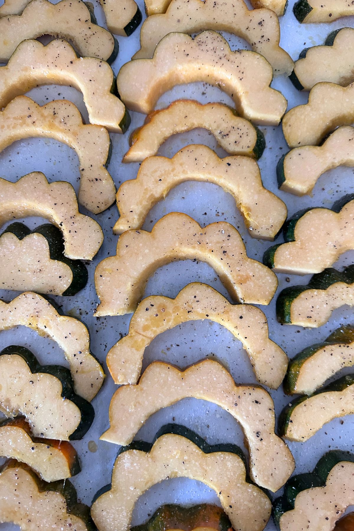 Acorn squash coated with maple syrup, salt, and pepper arranged on a parchment lined baking sheet in a single layer.