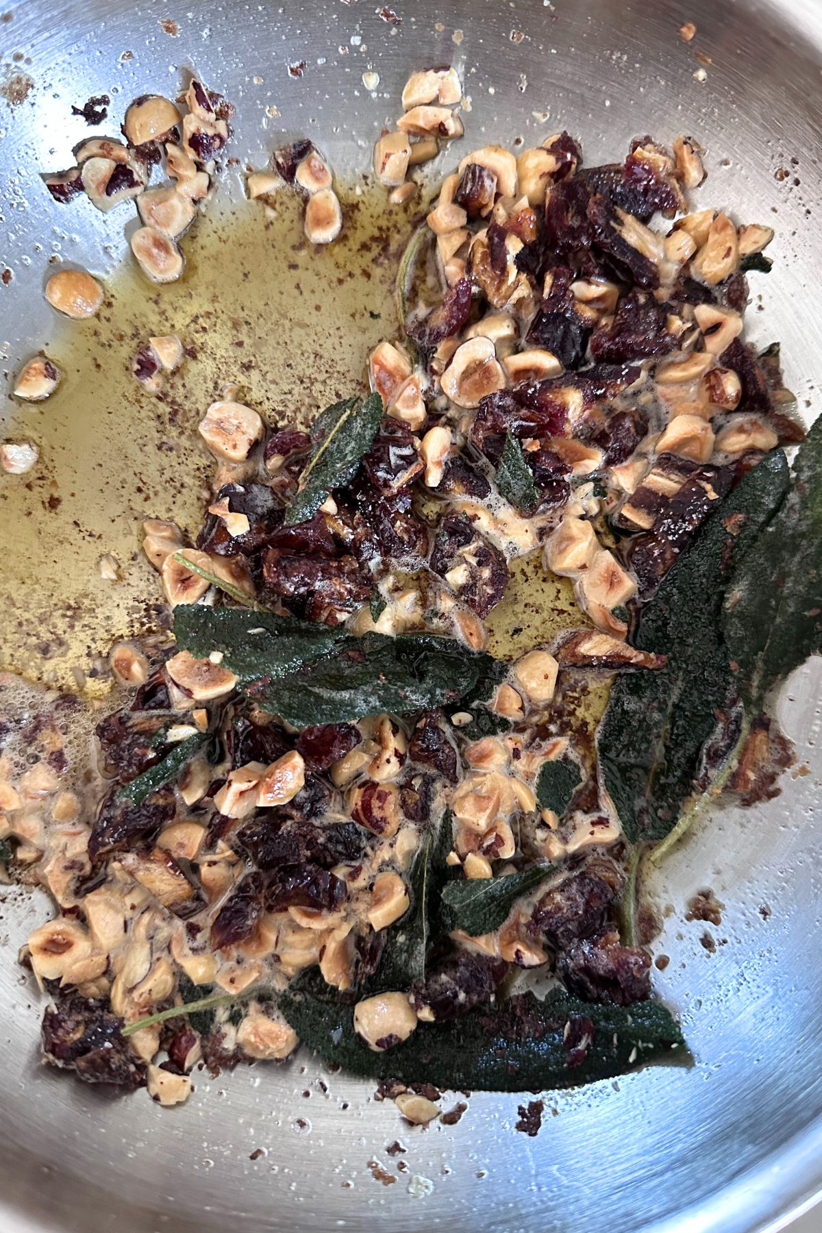 Melted butter in a large skillet with sage leaves, hazelnuts, and raisins simmering to make sage brown butter.