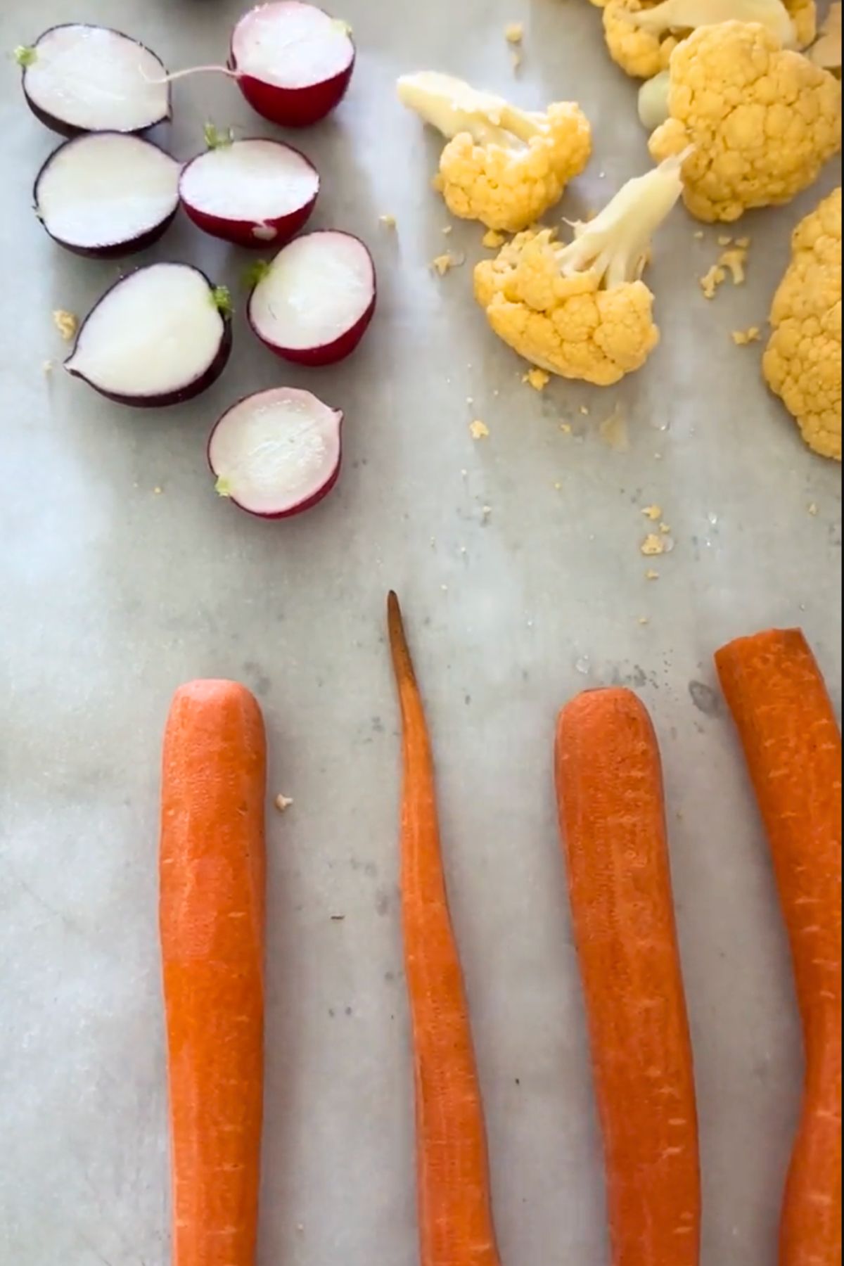 raw veggies on a cutting board including carrots, cauliflower, and radish