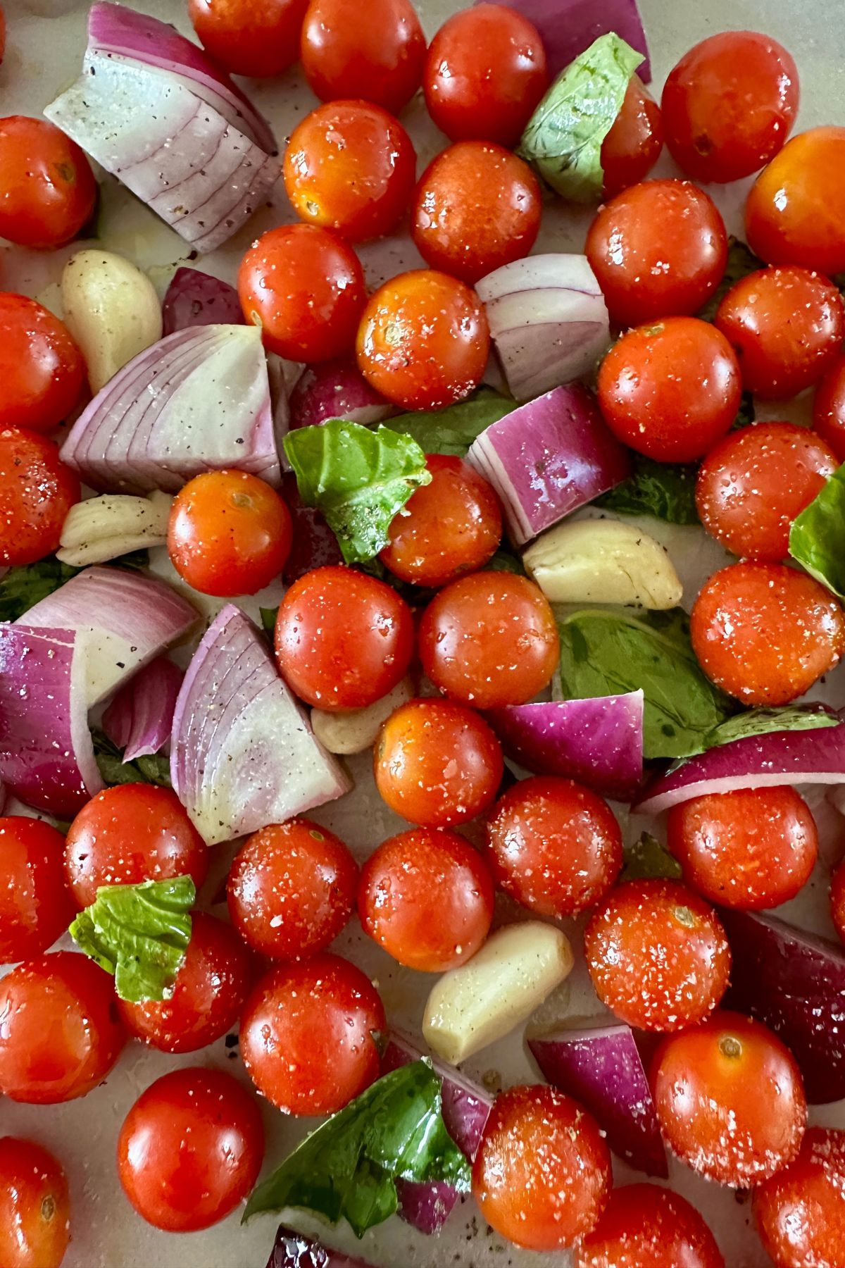 raw veggies on a baking sheet including cherry tomatoes, red onion, garlic and basil. 