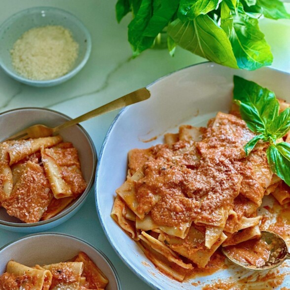 roasted tomato pasta served on a white plate with fresh basil and grated parmesan cheese.